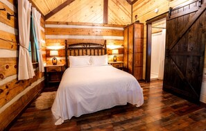 Une chambre à coucher de style cabane en bois, avec un lit, des tables de chevet et une porte de style grange.