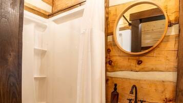 Ein Badezimmer einer Holzhütte mit Dusche, Waschbecken und Spiegel.