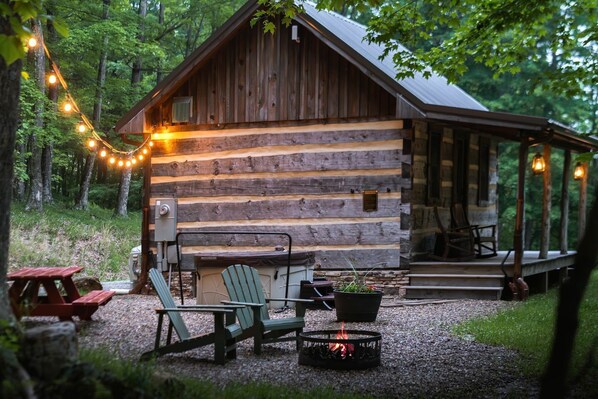 A rustic log cabin with a porch, outdoor seating, and a fire pit.