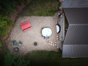 Vista aérea de un patio con un jacuzzi, un banco rojo y dos sillas verdes.