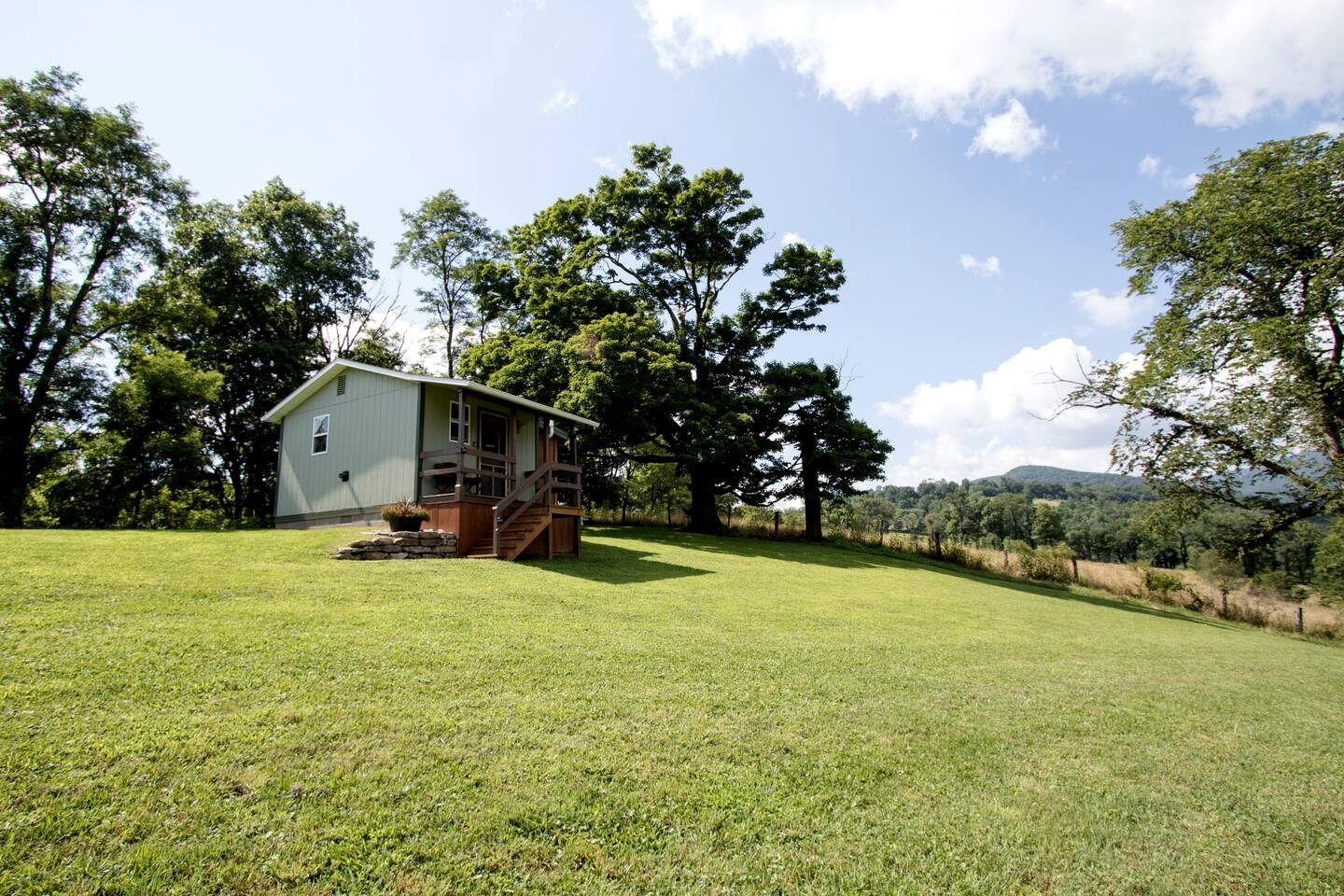A single-story house with a porch, surrounded by a grassy field and trees.