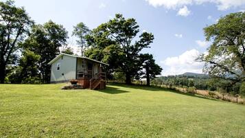 A single-story house with a porch, surrounded by a grassy field and trees.