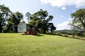 A single-story house with a porch, surrounded by a grassy field and trees. - Peaceful Tiny House in the Mountains near Seneca Rocks, West Virginia (Seneca Rocks)