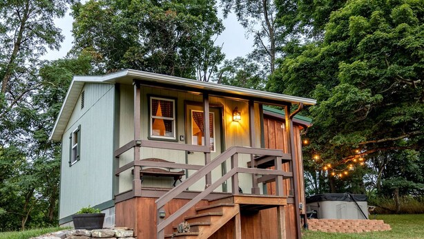 Une petite cabane avec une terrasse en bois, un mur en pierre et un escalier menant à un porche.