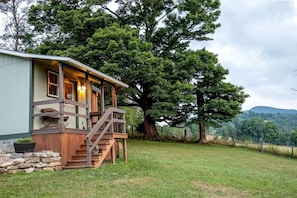 A cabin with a wooden deck, a staircase, and a large tree in the background.