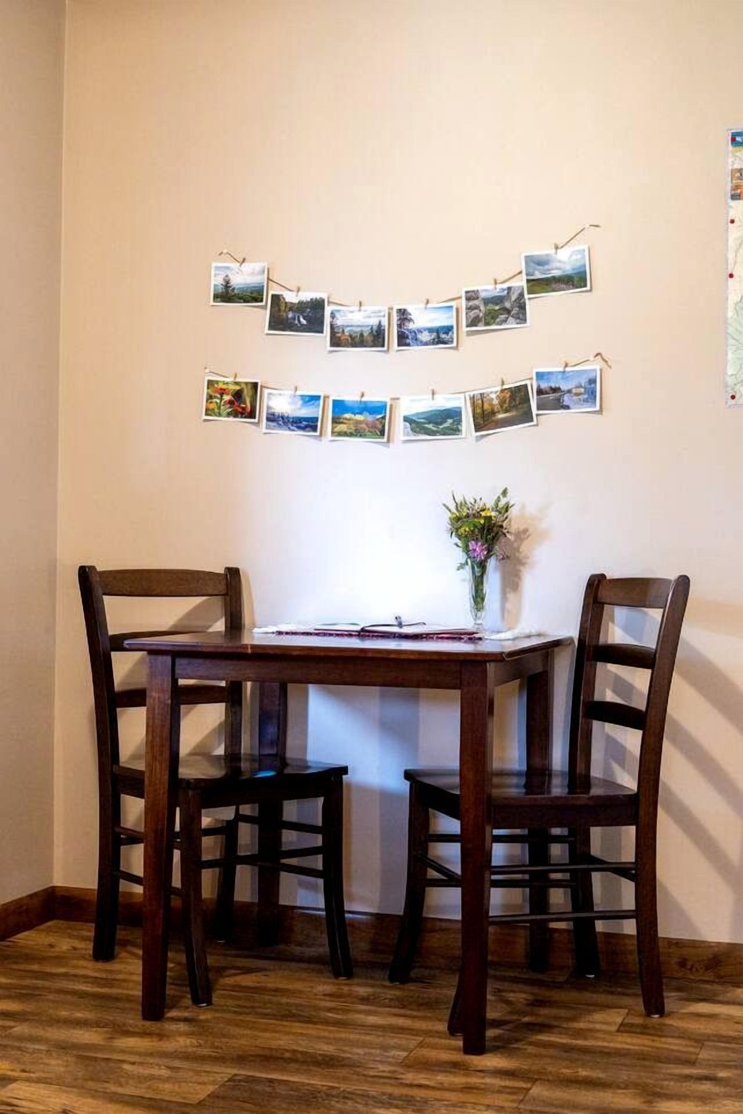 Un coin repas avec une table et des chaises en bois, un vase rempli de fleurs et une guirlande de photos accrochée au mur.