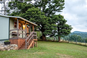 Une cabane dotée d’une terrasse en bois, d’un escalier et d’un grand arbre en arrière-plan.