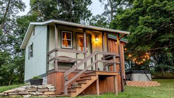 A small cabin with a wooden deck, a stone wall, and a staircase leading to a porch.