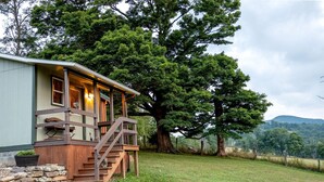 Une cabane dotée d’une terrasse en bois, d’un escalier et d’un grand arbre en arrière-plan.