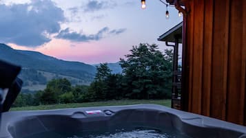 Un bain à remous avec une terrasse en bois, une vue sur les montagnes et des guirlandes lumineuses.