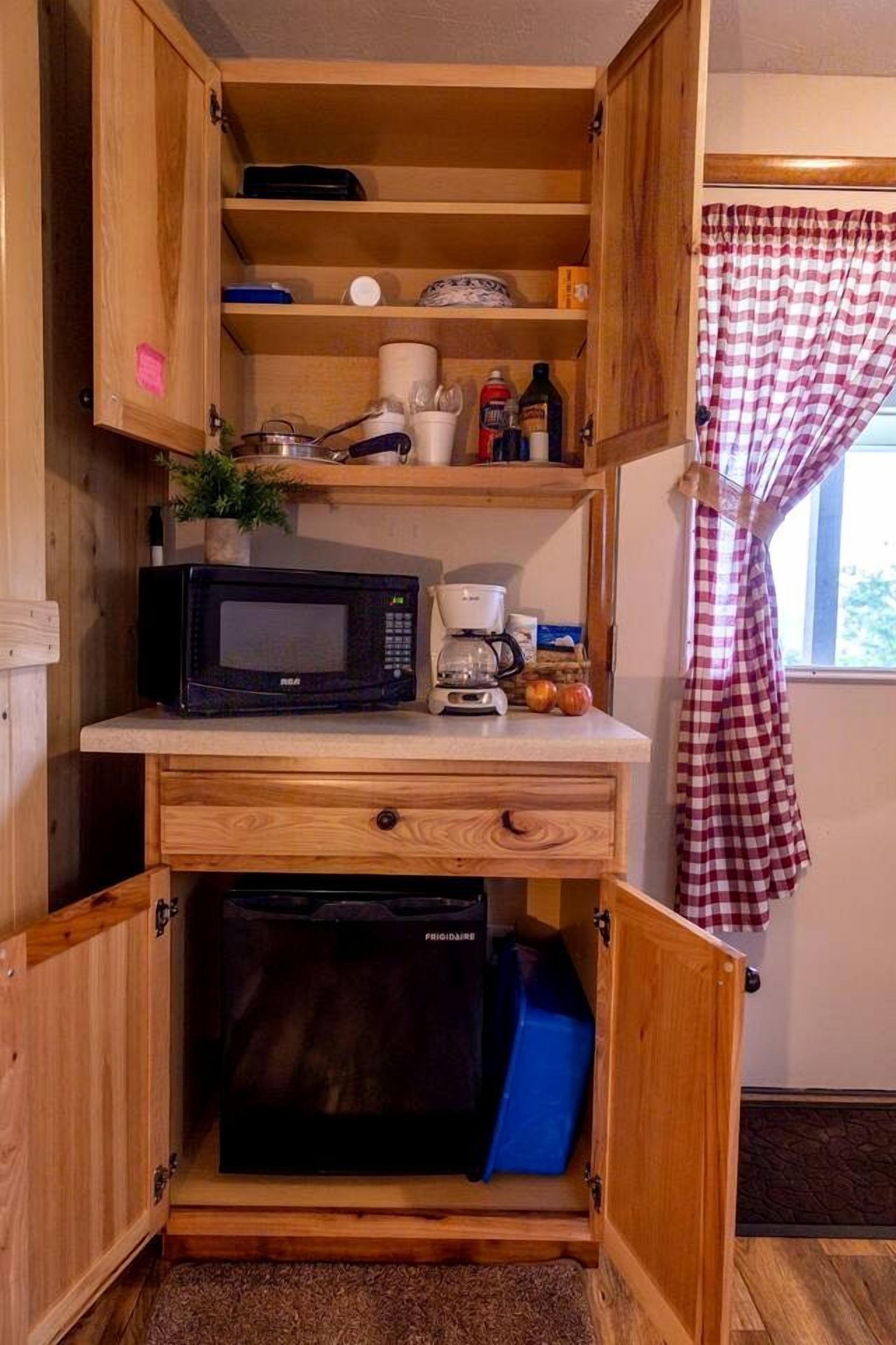 A compact kitchenette with a microwave, coffee maker, and storage cabinets.