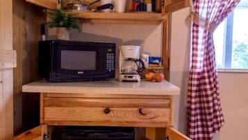 A compact kitchenette with a microwave, coffee maker, and storage cabinets.