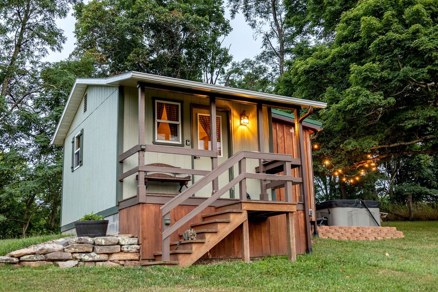 A small cabin with a wooden deck, a stone wall, and a staircase leading to a porch.