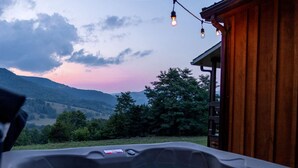 Un bain à remous avec une terrasse en bois, une vue sur les montagnes et des guirlandes lumineuses.