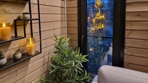 A wooden interior with a glass door leading outside, a shelf with candles, and a potted plant. - Borealis (Muonio)