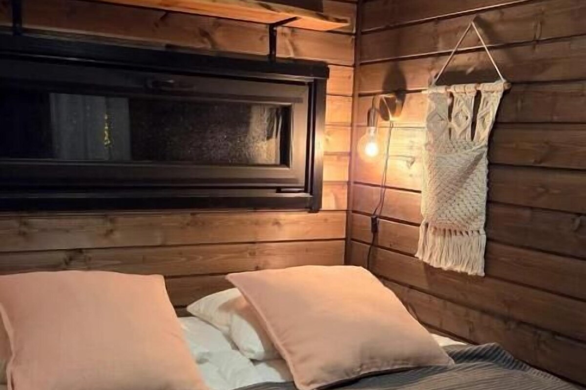A cozy cabin-style room with a bed, a window, and a hanging macrame wall decoration.