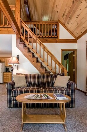 A cozy living room with a wooden staircase, a plaid sofa, a wooden coffee table, and a kitchen in the background. - Secluded West Virginia Cabin Rental on the Edge of Monongahela National Forest (Riverton)