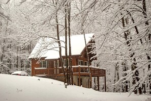 Una cabaña de madera con porche y techo cubierto de nieve.