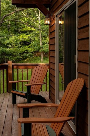 A wooden deck with two Adirondack chairs, a glass door, and a view of a forested area.