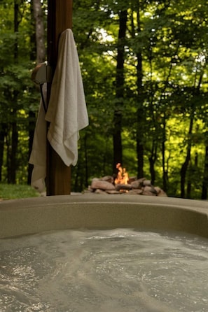 A hot tub in a forested area with a fire in the background.