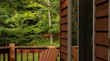 A wooden deck with two Adirondack chairs, a glass door, and a view of a forested area.