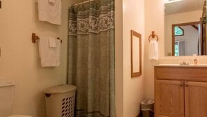 Un baño con inodoro, cortina de ducha, lavabo con espejo y un cubo de basura.