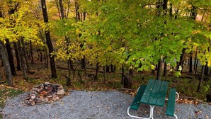 Zona de grava con una pila de rocas, una mesa de picnic verde y un fondo boscoso.