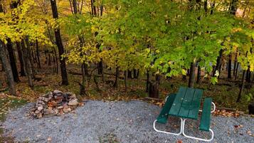 Et område med grus, en bunke sten, et grønt picnicbord og en skov i baggrunden.