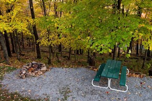 A gravel area with a stack of rocks, a green picnic table, and a forested background. - Secluded West Virginia Cabin Rental on the Edge of Monongahela National Forest (Riverton)