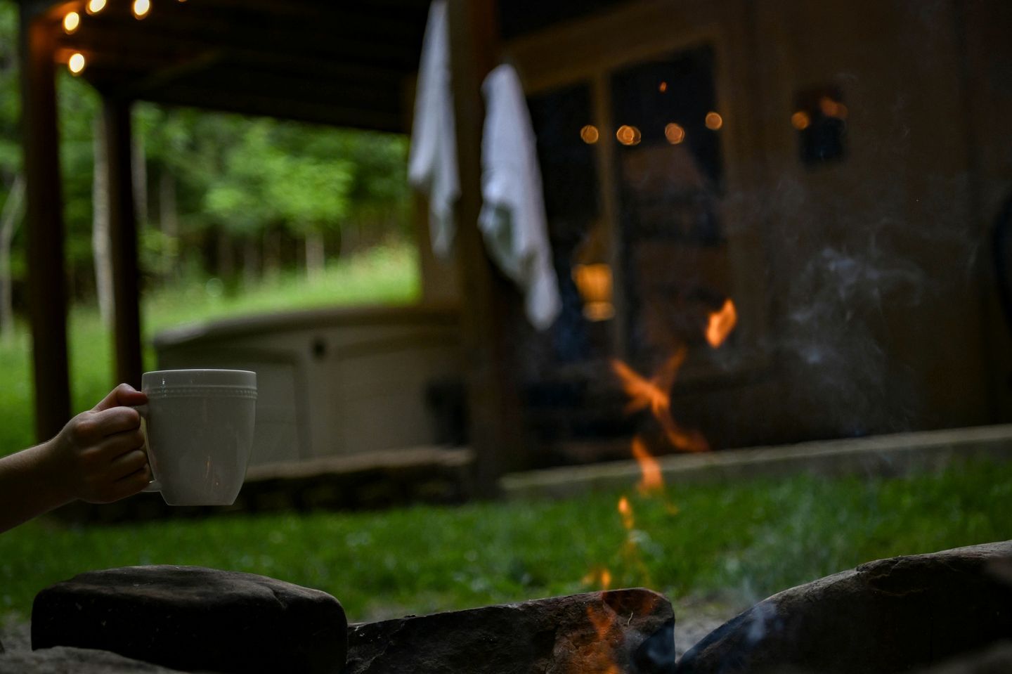 A person holding a cup, a fire, and a building with a porch.