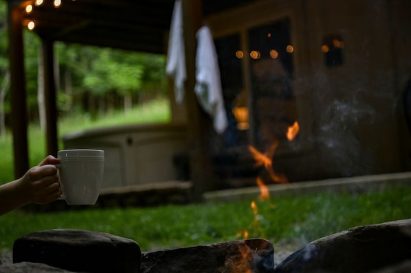 A person holding a cup, a fire, and a building with a porch.