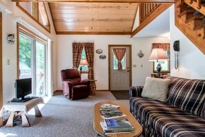 A cozy living room with a television, a recliner, a striped sofa, and a coffee table with books.