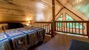 Un dormitorio con techo de madera, una cama con colcha, una mesita de noche y vistas al exterior desde un balcón.