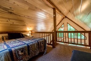 A bedroom with a wooden ceiling, a bed with a quilt, a nightstand, and a view of the outdoors through a balcony. - Secluded West Virginia Cabin Rental on the Edge of Monongahela National Forest (Riverton)