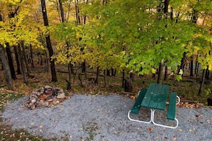 Une zone recouverte de gravier, avec un tas de pierres, une table de pique-nique verte et un paysage boisé en arrière-plan.