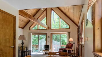A spacious room with a high ceiling, large windows, a dining area, and a cozy seating arrangement.
