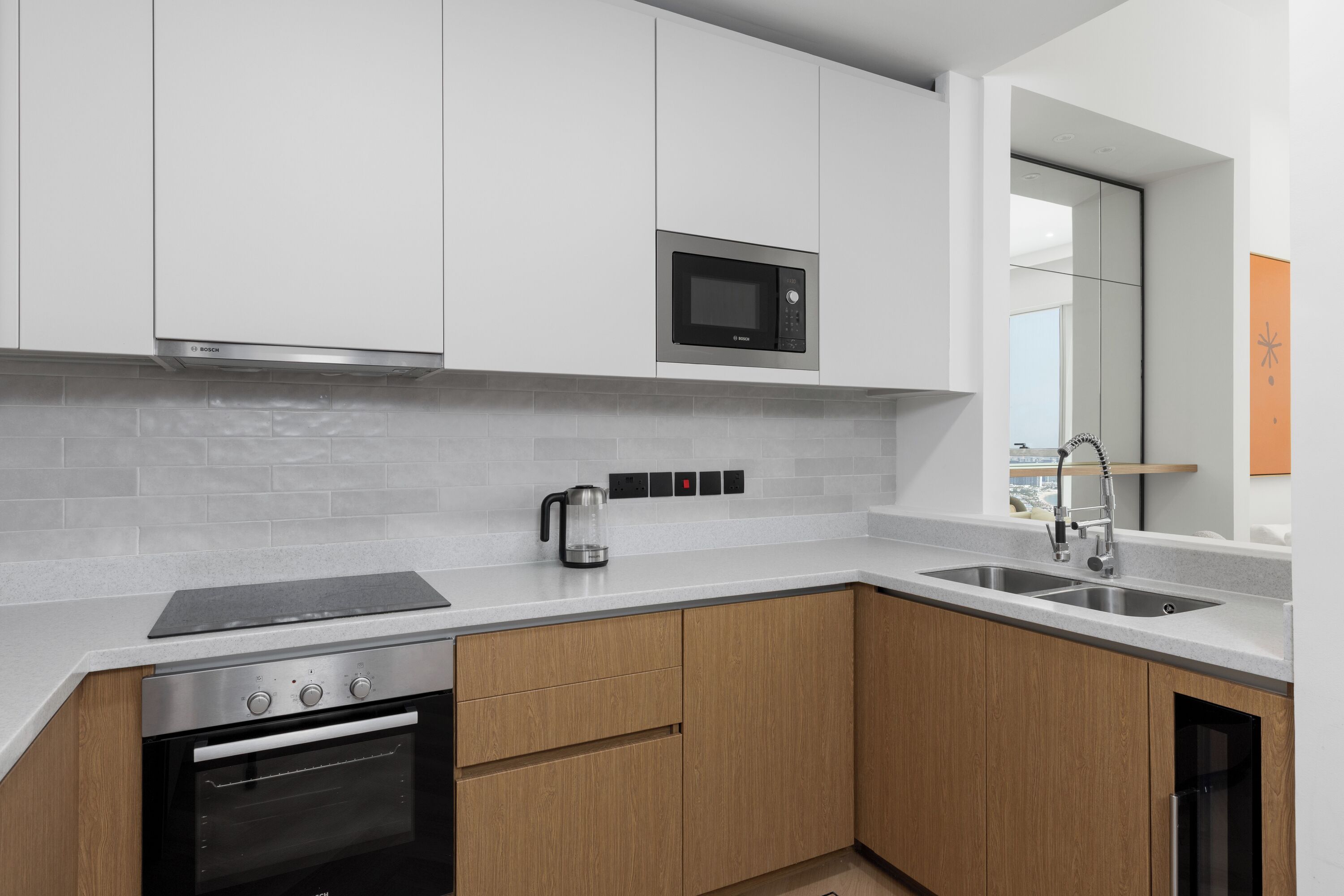 Een moderne keuken met witte kasten, een roestvrijstalen magnetron, een inbouwoven en een dubbele spoelbak.