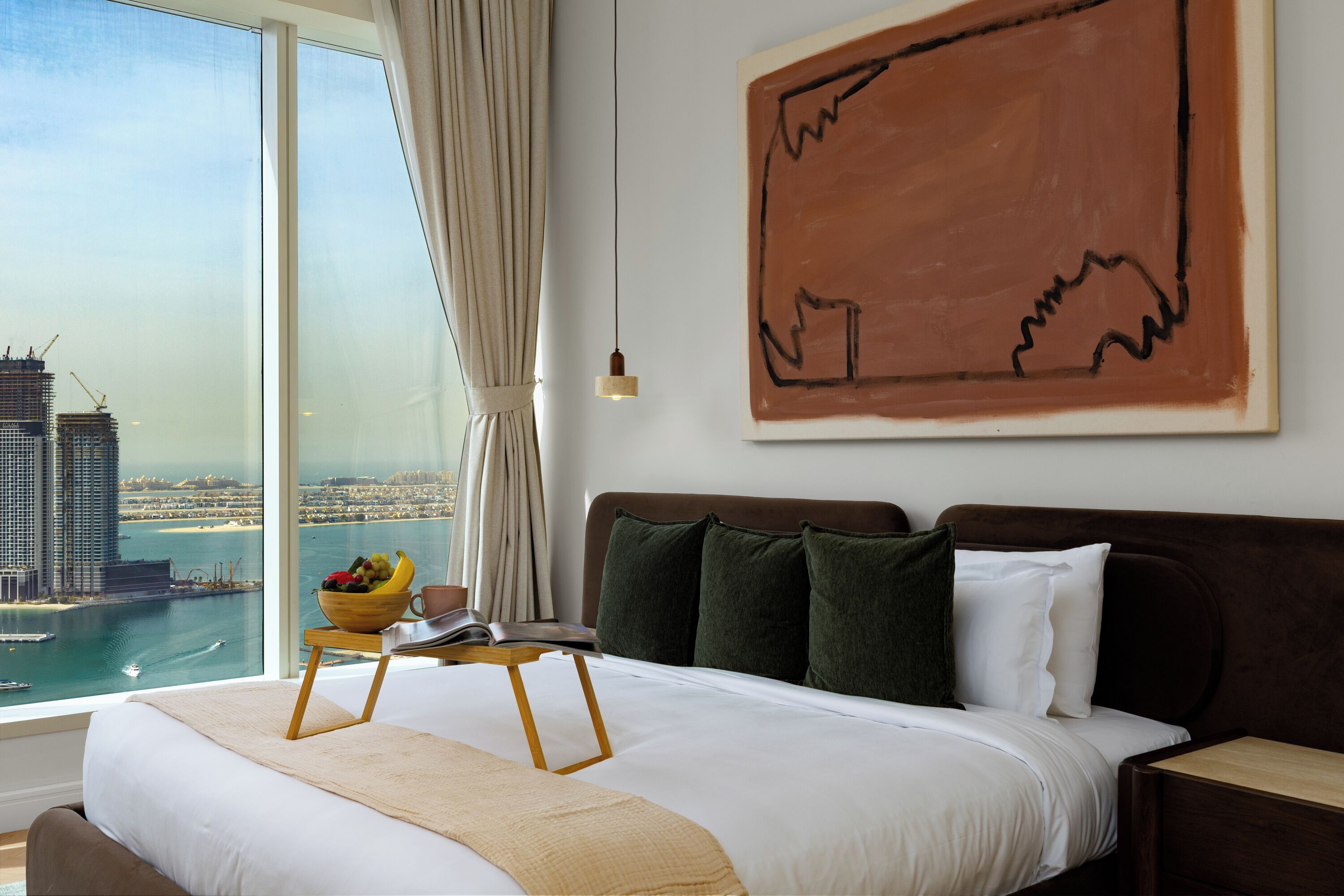 A hotel room with a large bed, a view of the city, and a painting on the wall.