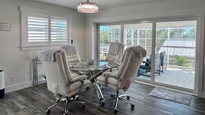 A conference room with a glass table, four chairs with fur throw blankets, a chandelier, and large windows with blinds. - Tropical Hideaway in Fort Myers Beach (Fort Myers Beach)
