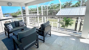 Ein sonniger Balkon mit einer Couch und einem Sessel, einer Uhr und Blick auf ein Sportfeld.