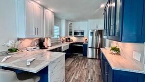 A modern kitchen with white and blue cabinets, a marble countertop, a stainless steel refrigerator, and a built-in oven. - Tropical Hideaway in Fort Myers Beach (Fort Myers Beach)