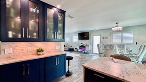 A modern kitchen with dark blue cabinets, a marble countertop, and a dining area with a table and chairs. - Tropical Hideaway in Fort Myers Beach (Fort Myers Beach)