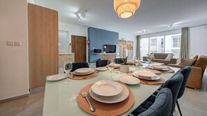 Un comedor moderno con una mesa de vidrio, platos, cubiertos y una lámpara colgante.