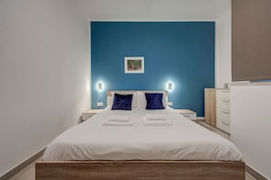 Une chambre d’hôtel avec un grand lit, deux tables de chevet, une petite table, une commode et un tableau accroché au mur.