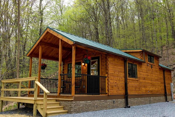 A wooden cabin with a porch, stone foundation, and a metal roof.