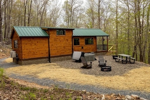A cabin with a green roof, a porch with a railing, and outdoor seating with a fire pit.