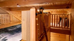 A wooden interior with a staircase, a bed with pillows, and a small plant.