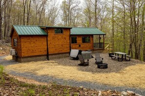 A cabin with a green roof, a porch with a railing, and outdoor seating with a fire pit.