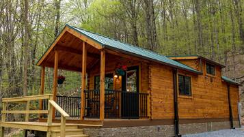 A wooden cabin with a porch, stone foundation, and a metal roof.