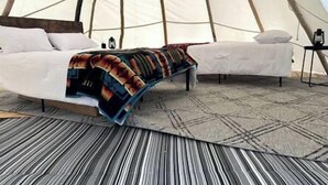 Een tent met twee bedden, een kamerkleed met dessin en een deken.